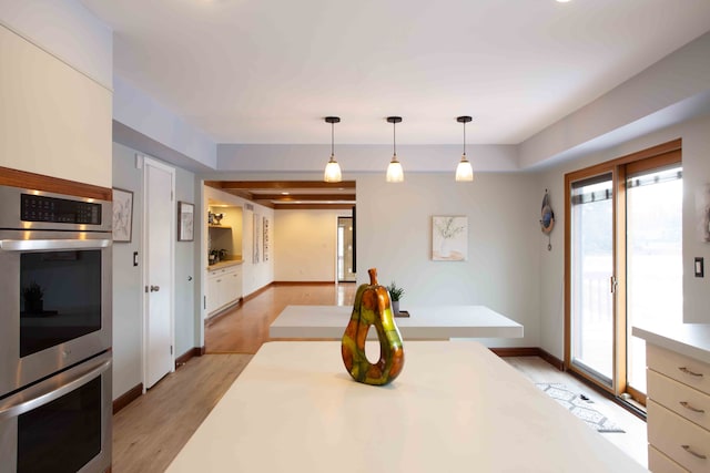 kitchen featuring white cabinetry, decorative light fixtures, light hardwood / wood-style floors, and stainless steel double oven