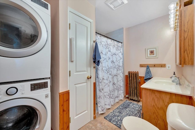 washroom featuring stacked washer / dryer, radiator, and sink