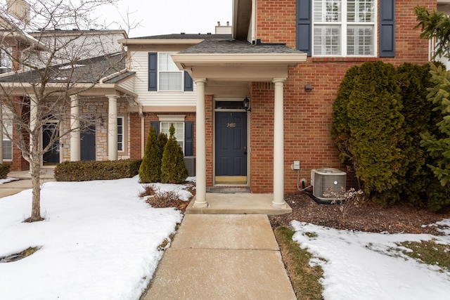 snow covered property entrance featuring central AC unit