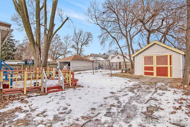 snowy yard featuring a wooden deck, a storage shed, and a trampoline