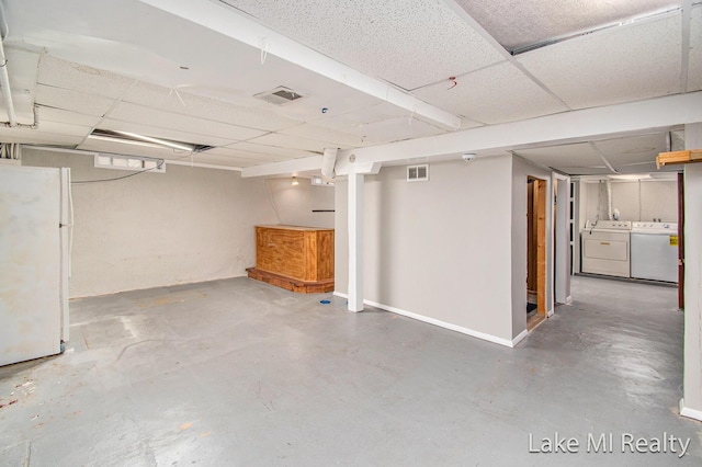 basement with a drop ceiling, washer and dryer, and white fridge