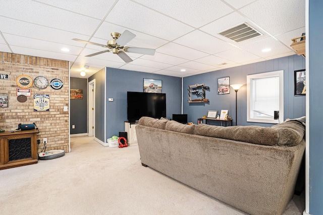 carpeted living room featuring brick wall, a drop ceiling, and ceiling fan