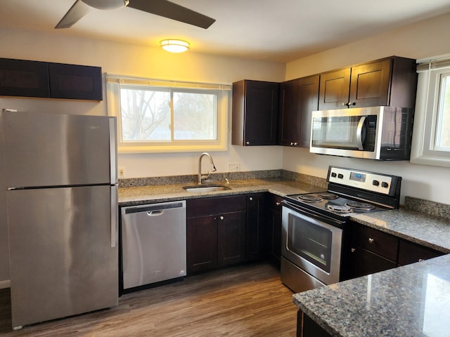 kitchen with stone counters, appliances with stainless steel finishes, sink, ceiling fan, and light wood-type flooring