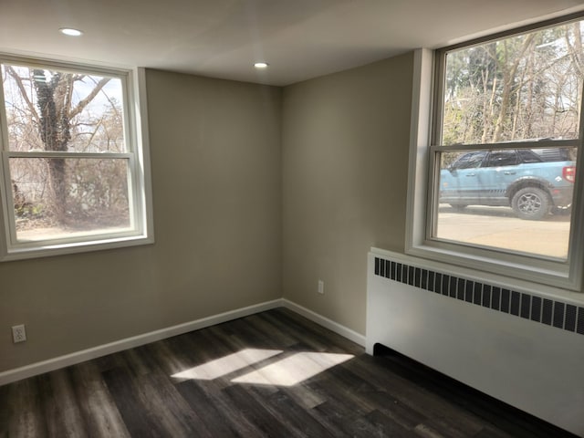 unfurnished room with radiator, dark wood-type flooring, and a healthy amount of sunlight