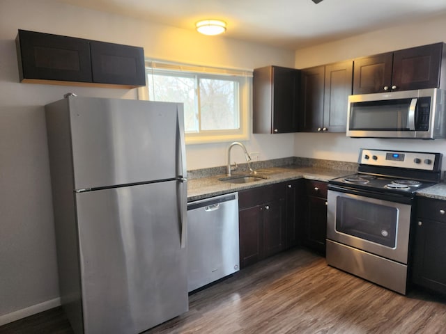 kitchen with sink, dark hardwood / wood-style flooring, light stone counters, stainless steel appliances, and dark brown cabinets