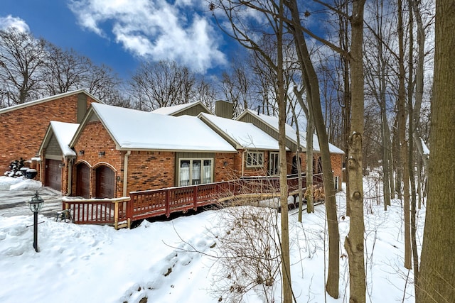 snow covered property with brick siding, french doors, and a wooden deck