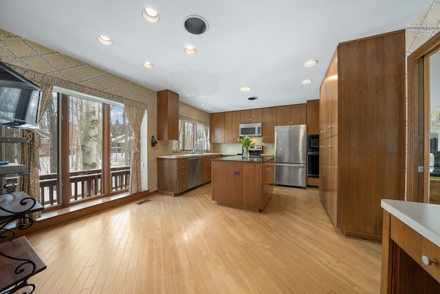 kitchen featuring brown cabinets, stainless steel appliances, light wood finished floors, and a center island
