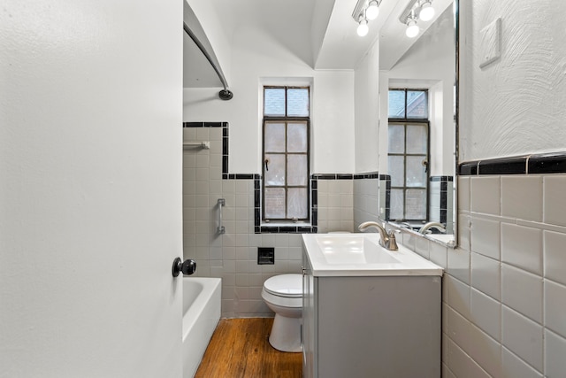 full bathroom with shower / washtub combination, hardwood / wood-style floors, tile walls, vanity, and toilet