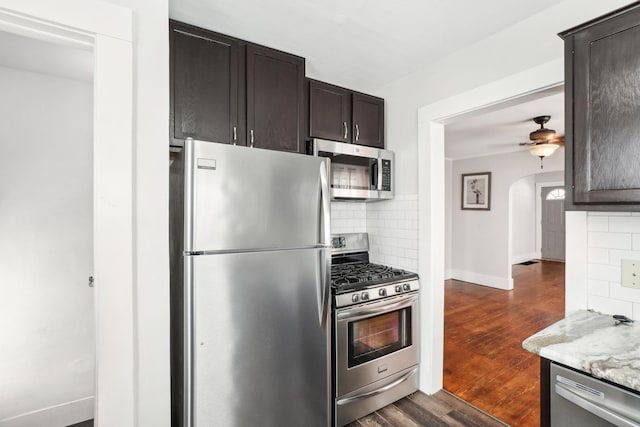 kitchen featuring light stone counters, dark brown cabinets, appliances with stainless steel finishes, decorative backsplash, and dark wood-style floors