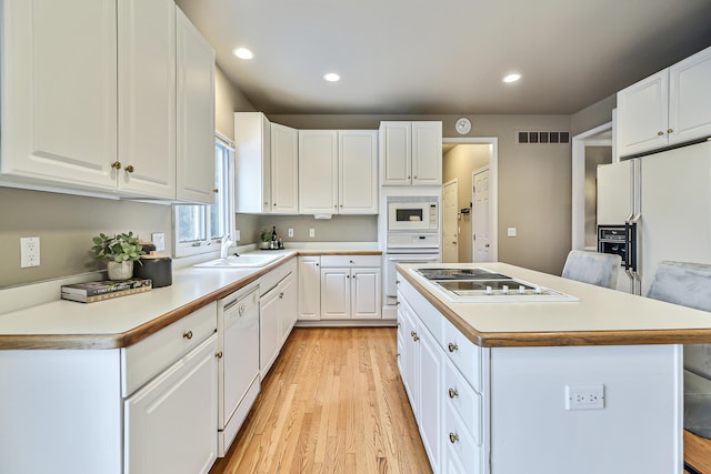 kitchen with a kitchen island, sink, white cabinets, light hardwood / wood-style floors, and white appliances