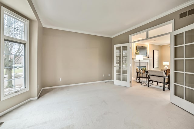 empty room with a tiled fireplace, crown molding, french doors, and carpet