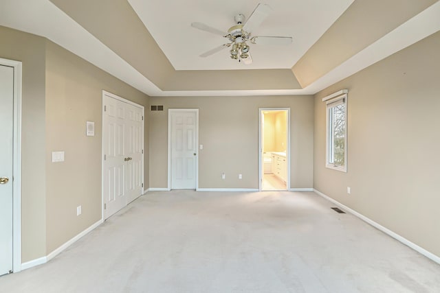 unfurnished bedroom with ceiling fan, light colored carpet, connected bathroom, and a raised ceiling