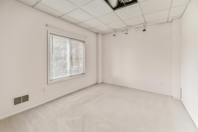 empty room with a paneled ceiling, rail lighting, and light carpet