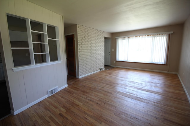 spare room with brick wall and hardwood / wood-style floors