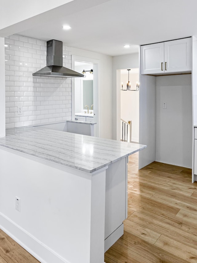 kitchen with white cabinetry, light stone counters, light hardwood / wood-style flooring, kitchen peninsula, and wall chimney range hood