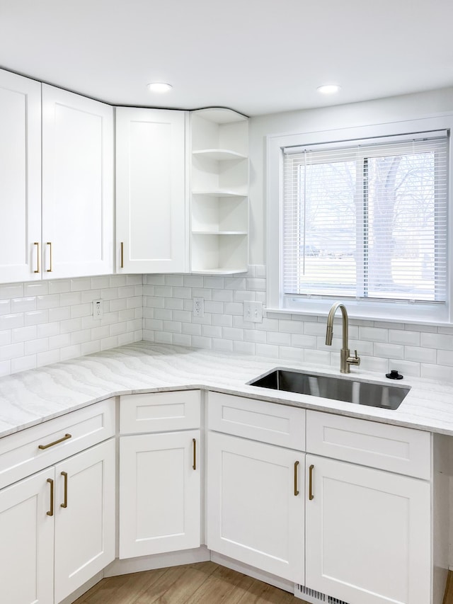 kitchen with white cabinetry, sink, light stone counters, and backsplash