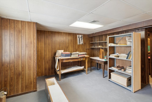 interior space featuring wooden walls, concrete floors, and a drop ceiling