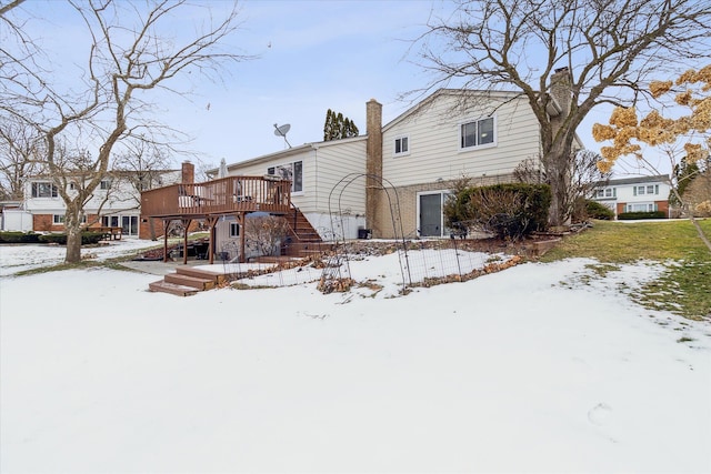 snow covered house featuring brick siding, a wooden deck, and stairs