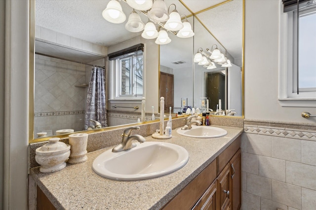 full bathroom featuring a textured ceiling, a sink, visible vents, and tile walls