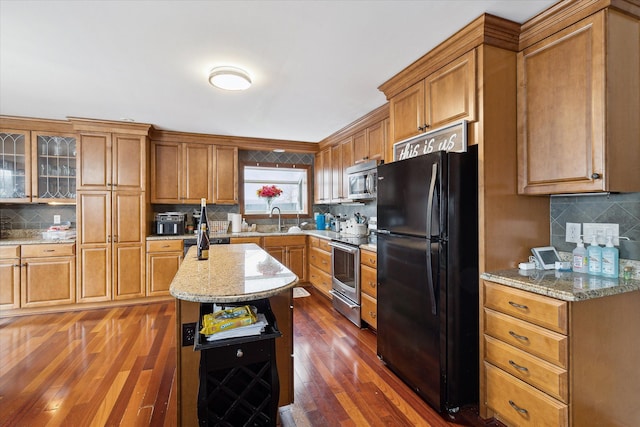 kitchen with brown cabinetry, dark wood finished floors, decorative backsplash, stainless steel appliances, and a sink