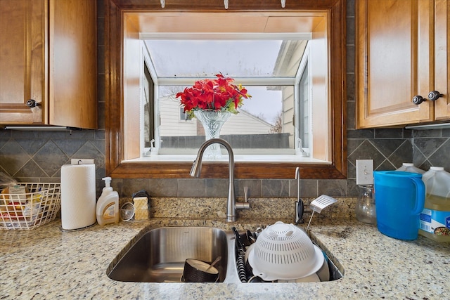 interior details featuring brown cabinetry, a sink, backsplash, and light stone countertops