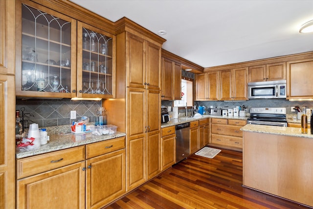 kitchen with light stone counters, stainless steel appliances, backsplash, dark wood finished floors, and glass insert cabinets