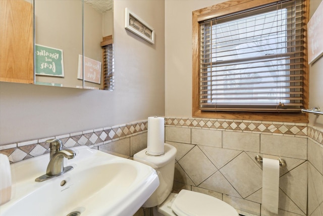 bathroom with toilet, tile walls, a sink, and wainscoting