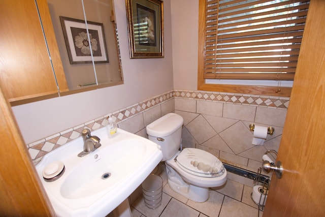 bathroom with tile walls, toilet, wainscoting, a sink, and tile patterned floors