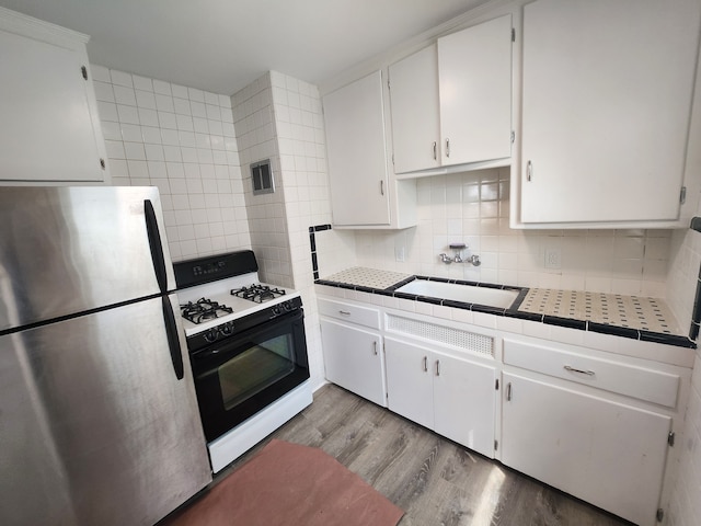 kitchen featuring sink, white cabinetry, stainless steel refrigerator, gas range oven, and backsplash