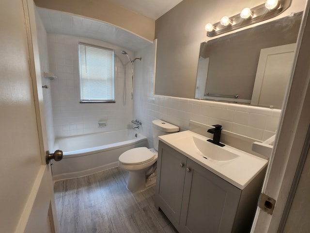 full bathroom with tile walls, hardwood / wood-style floors, tiled shower / bath combo, vanity, and toilet