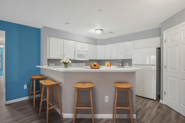 kitchen with white appliances, white cabinets, dark hardwood / wood-style flooring, a kitchen bar, and kitchen peninsula