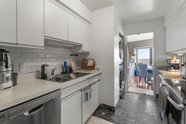 kitchen featuring sink, appliances with stainless steel finishes, backsplash, stacked washer and clothes dryer, and white cabinets