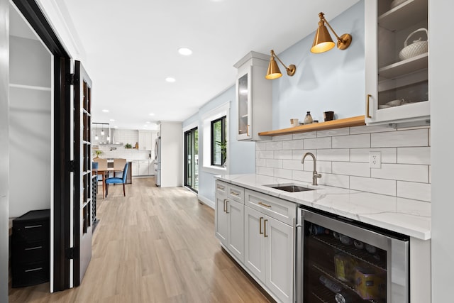 kitchen featuring wine cooler, sink, stainless steel refrigerator, light stone countertops, and white cabinets