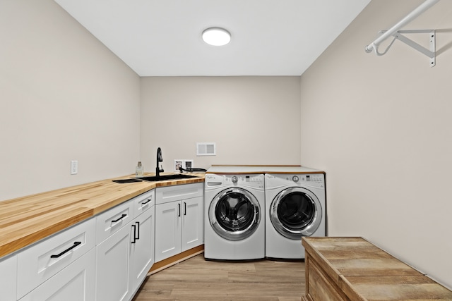 clothes washing area featuring sink, light hardwood / wood-style flooring, washing machine and dryer, and cabinets