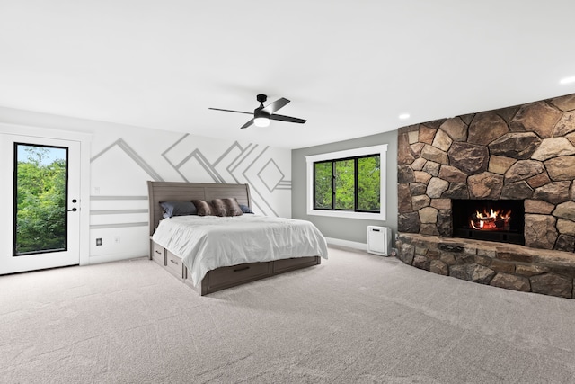 carpeted bedroom with a stone fireplace, access to outside, and ceiling fan