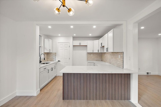 kitchen featuring sink, light stone counters, light hardwood / wood-style flooring, kitchen peninsula, and white cabinets