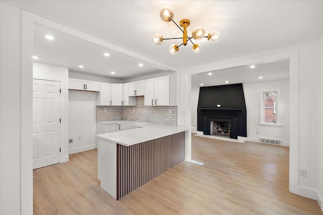 kitchen featuring backsplash, white cabinets, kitchen peninsula, light stone countertops, and light wood-type flooring