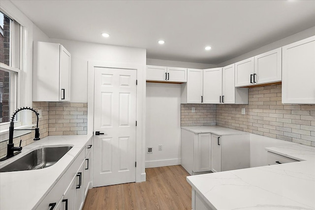 kitchen with white cabinetry, light stone countertops, sink, and light hardwood / wood-style flooring