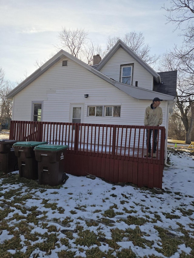 snow covered rear of property with a chimney and a wooden deck