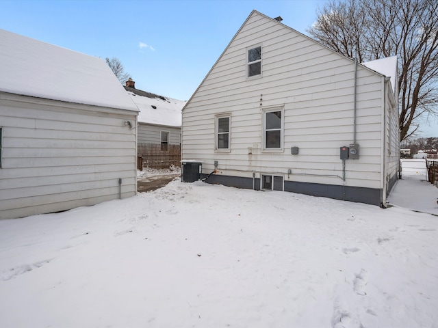 snow covered rear of property with cooling unit and fence