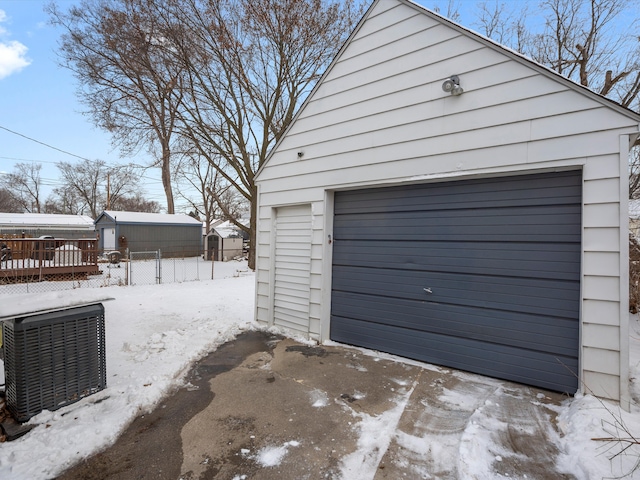 snow covered garage with a detached garage, fence, and central AC unit