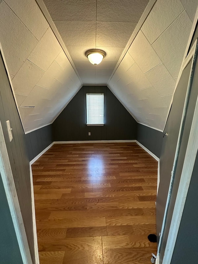 bonus room with vaulted ceiling, wooden walls, hardwood / wood-style floors, and a textured ceiling