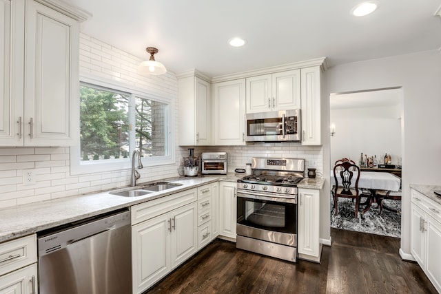 kitchen featuring sink, appliances with stainless steel finishes, dark hardwood / wood-style floors, light stone counters, and decorative backsplash