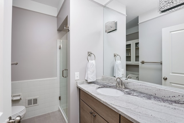 bathroom with toilet, a shower with shower door, tile walls, vanity, and tile patterned flooring