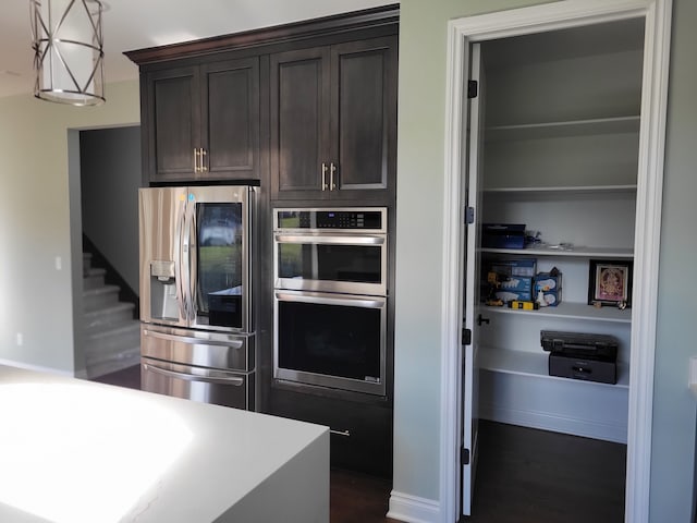 kitchen featuring dark brown cabinetry, decorative light fixtures, dark wood-type flooring, and appliances with stainless steel finishes