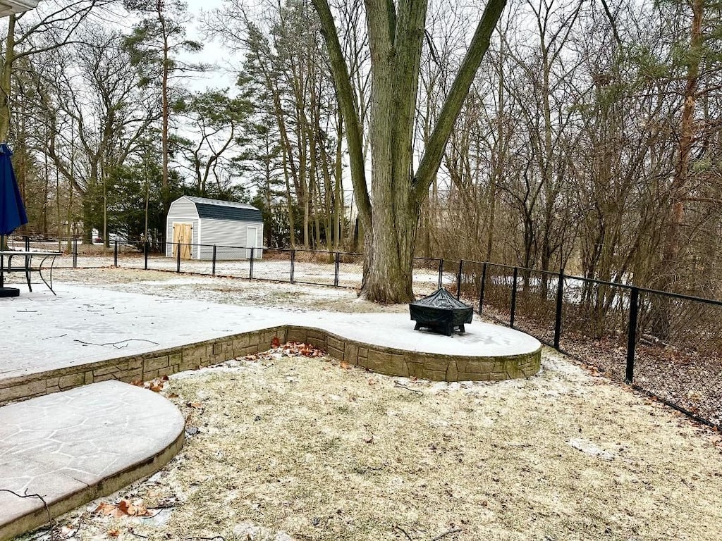 yard covered in snow with an outdoor fire pit and a shed