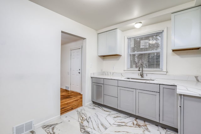 kitchen featuring light stone counters, sink, and gray cabinets