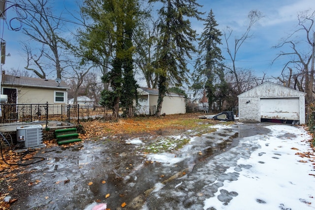 yard covered in snow with cooling unit, a garage, and an outbuilding