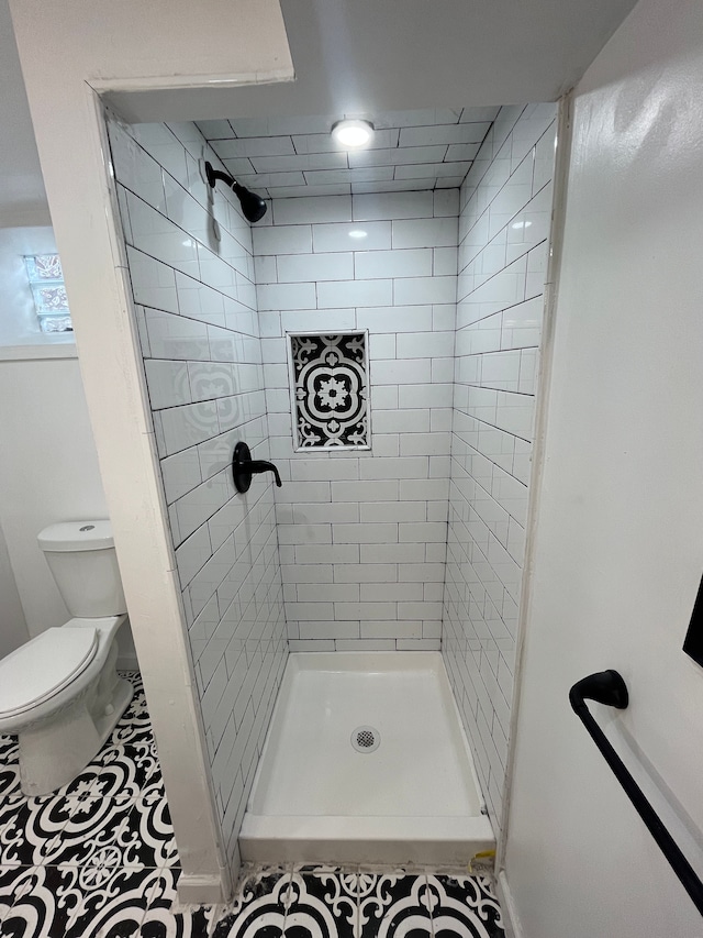 bathroom featuring a tile shower, tile patterned floors, and toilet