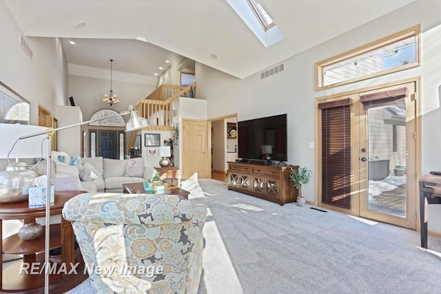 carpeted living room featuring a chandelier, high vaulted ceiling, and a skylight